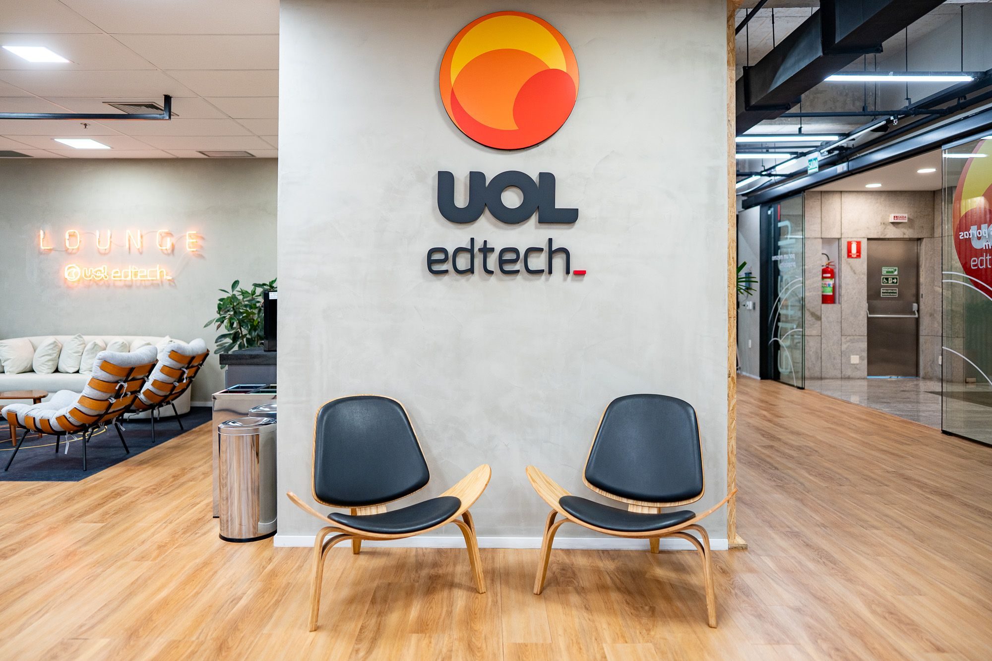 Parede de identidade visual da UOL EdTech, com letreiro do lounge e poltronas
